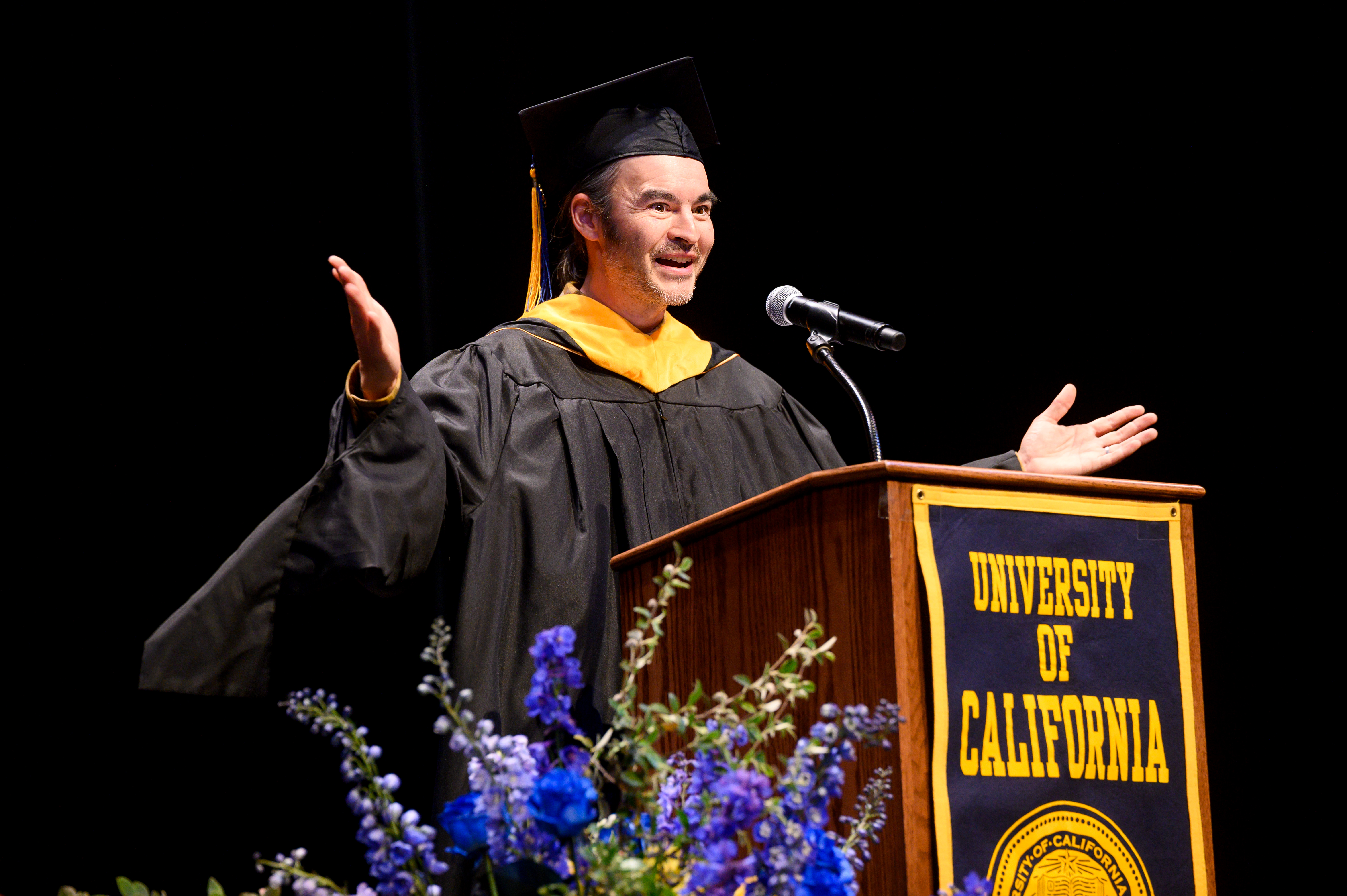 photo of Ken-ichi Ueda speaking at a podium in graduation regalia