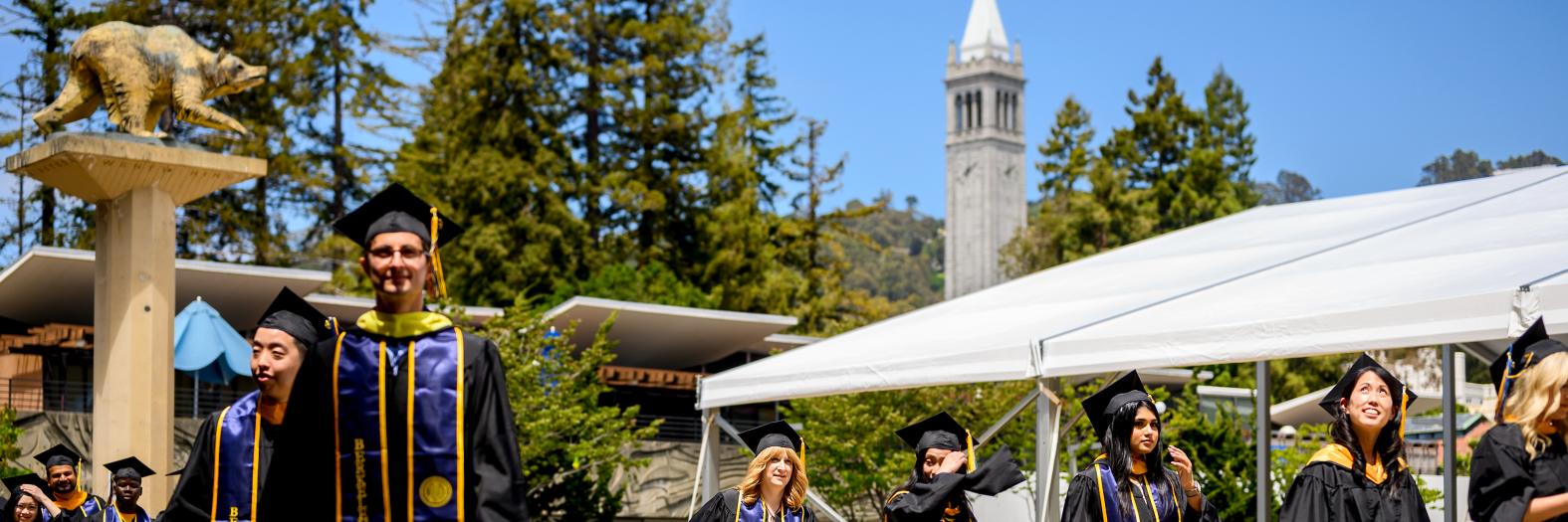 image of graduates walking outside, Campanile tower and a blue sky in the backgroun