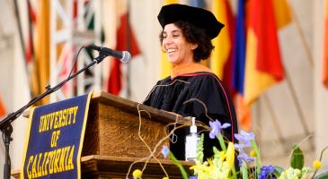 photo of Timnit Gebru in graduation regalia standing at a podium smiling