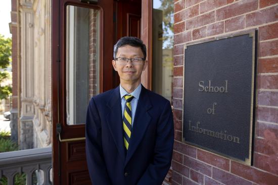 professor Chuang stands in front of South Hall next to a sign reading "School of Information"