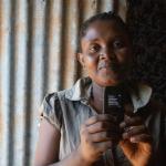 photo of a girl holding a mobile phone reading "You have received your Give Directly payment..."