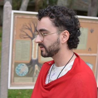 Boaz Kaufman looking serenely towards the left, wearing a floral shirt and red poncho with greenery in the background