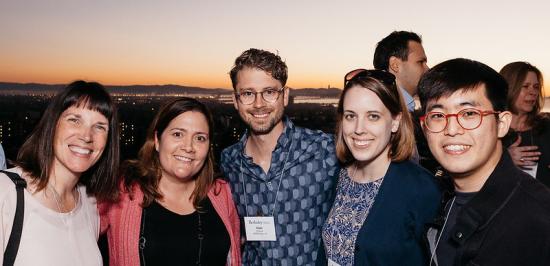 Photo of 5 people smiling for the camera with nighttime view of the city of Berkeley in the background